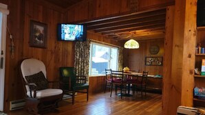 Um interior em madeira com área de jantar, televisão e janela com cortinas.