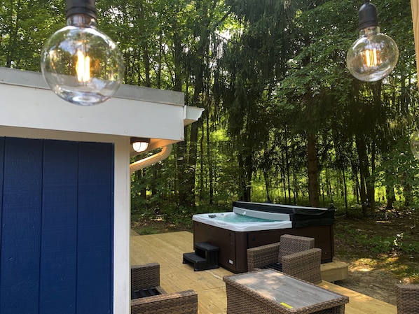 Une terrasse extérieure dotée d’un jacuzzi, de meubles en osier et de luminaires suspendus.