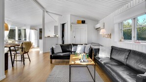 Ett modernt vardagsrum med en svart lädersoffa, ett träbord och en matplats med bord och stolar.