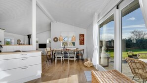 Ett modernt kök med vita skåp, en matplats med ett träbord och stolar samt en stor skjutdörr i glas som leder ut till en uteplats.