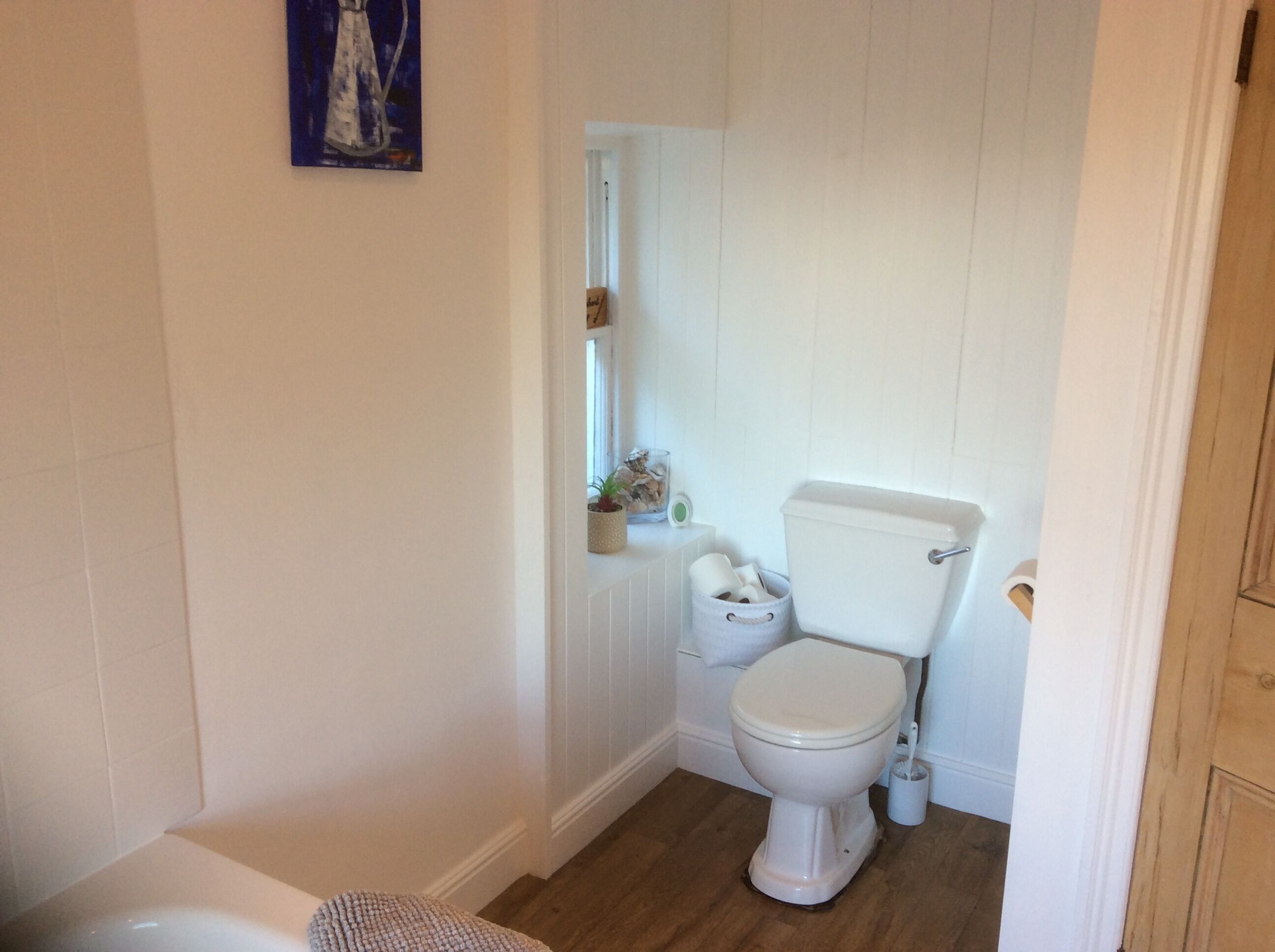 A small, white bathroom with a toilet, a small sink, and a wooden floor.