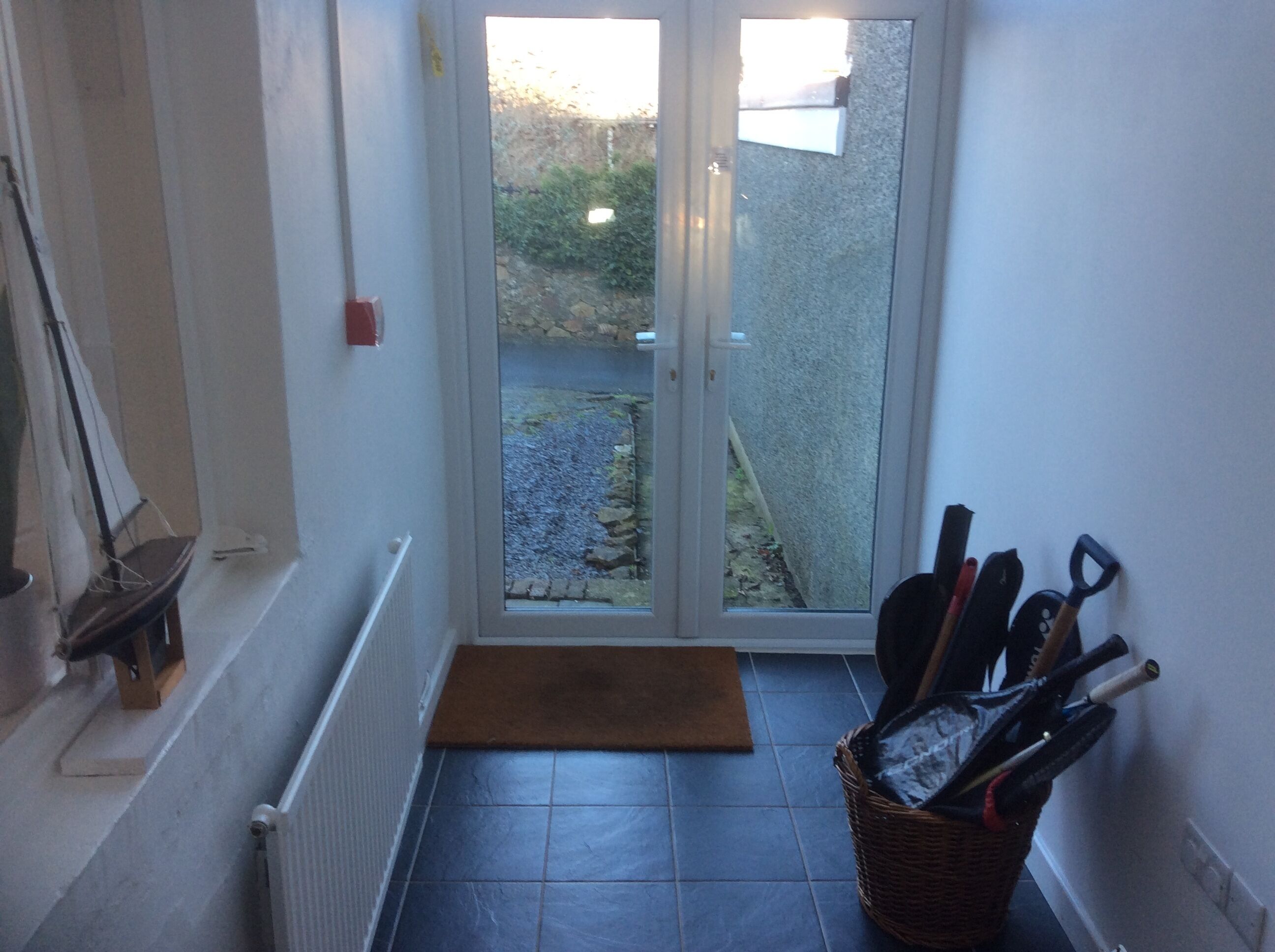 A narrow hallway with a door leading to a garden. A wicker basket with tools is placed against the wall.