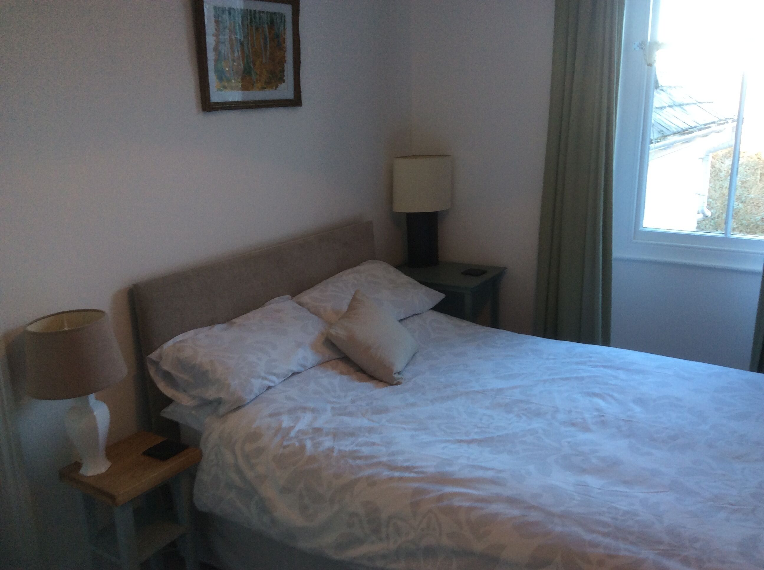 A neatly made bed with two pillows, a bedside lamp, and a small table with a lamp.
