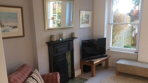 A living room with a fireplace, a television on a stand, a couch, and a window with a view of the outside. - Lovely 4-bed Victorian House in Bangor by the sea (Bangor)