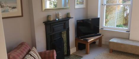 A living room with a fireplace, a television on a stand, a couch, and a window with a view of the outside.