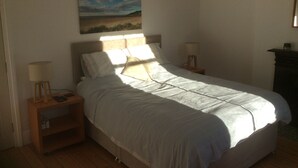 A bedroom with a bed, two bedside tables with lamps, a nightstand, and a painting on the wall. - Lovely 4-bed Victorian House in Bangor by the sea (Bangor)