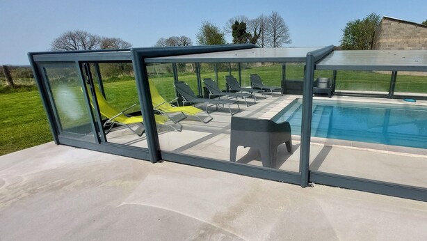 A covered outdoor area with a pool, lounge chairs, and a glass enclosure.
