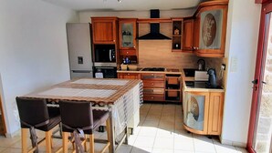 A compact kitchen with wooden cabinets, a built-in oven, and a dining area with two chairs.