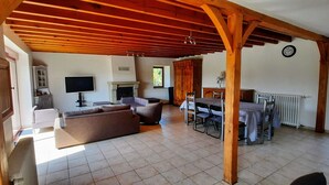 A spacious living area with a wooden ceiling, a fireplace, a television, and a dining table with chairs.