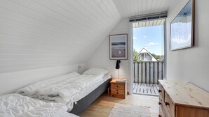 Un dormitorio con cama, mesita de noche, cómoda y ventana con vista a una casa.