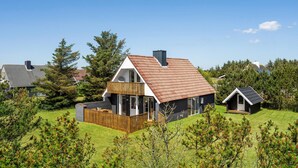 Una casa moderna con techo inclinado, terraza de madera y patio cercado.