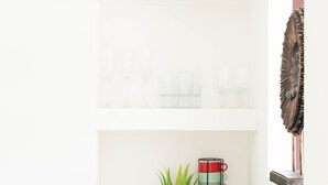 Una estantería blanca con adornos, incluyendo una planta en maceta, cristalería y un jarrón colorido.