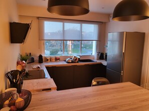 Uma cozinha moderna com uma janela grande, ilha integrada e frigorífico de aço inoxidável.