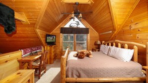 Accogliente camera da letto in una baita di legno, con un letto di legno, una televisione, una scrivania e una finestra vista alberi.