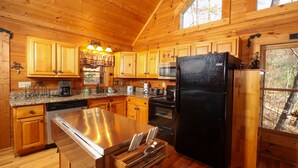 Una cucina in baita di legno con mobili in legno, elettrodomestici in acciaio inossidabile e una grande isola con lavello e portacoltelli.
