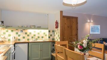 A kitchen with a tiled backsplash, wooden cabinets, a refrigerator, a sink, and a dining area with a table and chairs.
