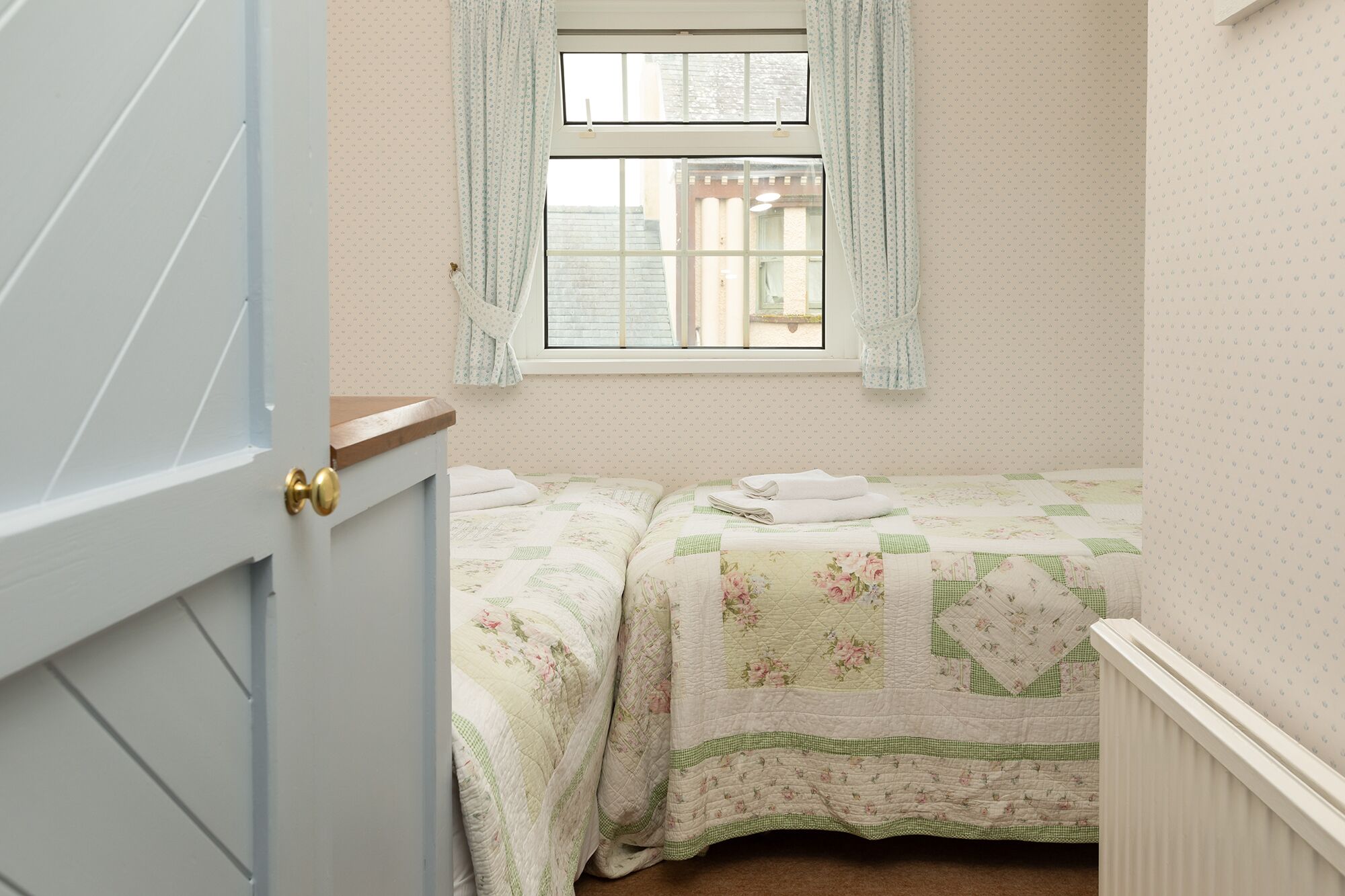 Een slaapkamer met twee bedden, een raam met gordijnen en een radiator.