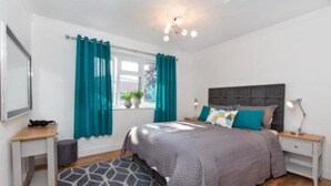 A bedroom with a bed, nightstands, a desk, a window with curtains, and a patterned rug. - Beautiful 1-bed Apartment in York Near Gym (York)