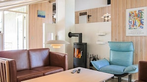 Ein gemütlicher Raum mit einem braunen Ledersofa, einem blauen Sessel, einem kleinen Tisch, einem Kaminofen und einem gerahmten Bild an der Wand.