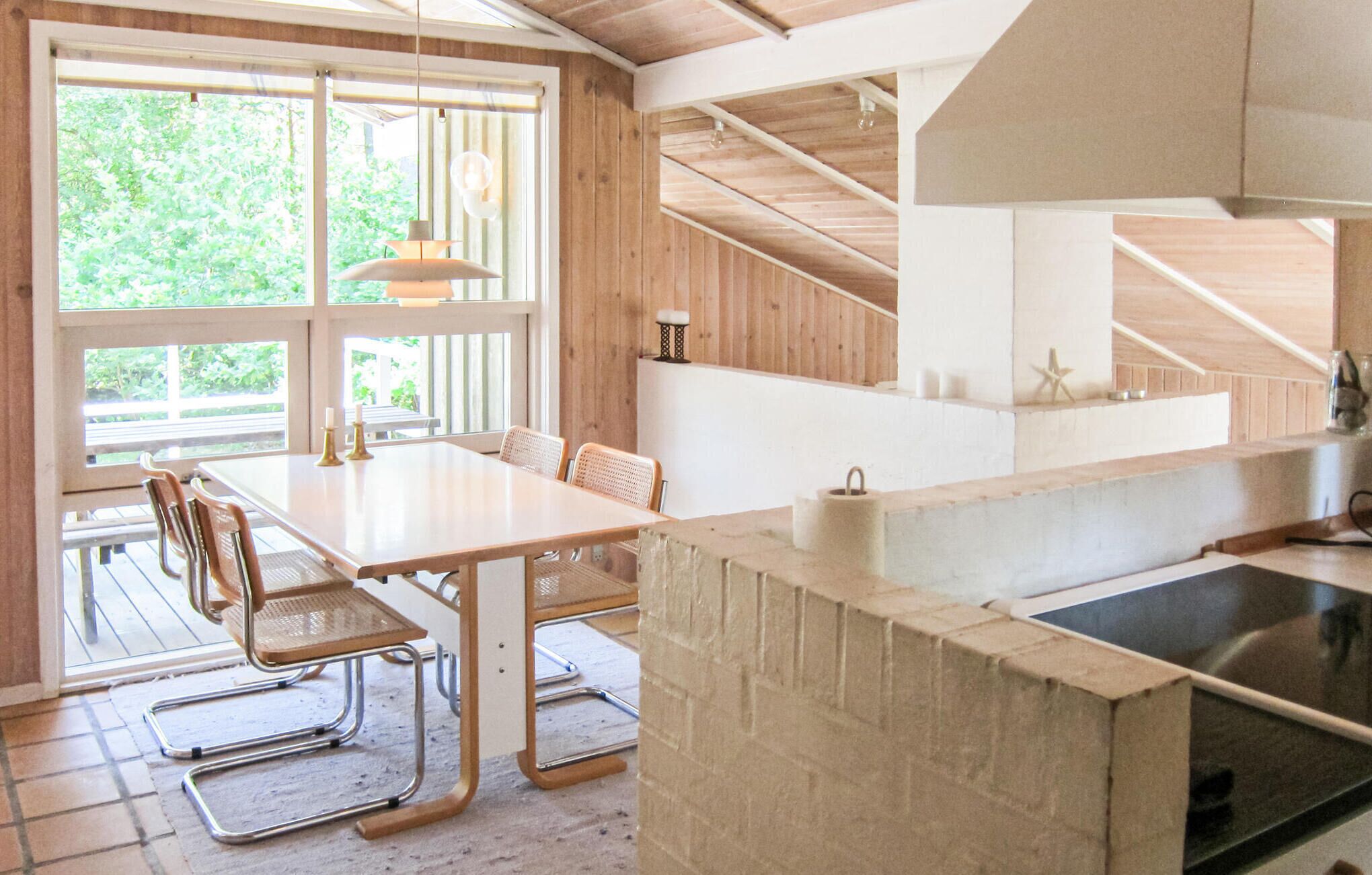 A modern kitchen with a wooden interior, a dining area with a table and chairs, and a large window providing natural light.