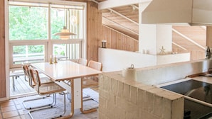 Eine moderne Küche mit Holzvertäfelung, ein Essbereich mit Tisch und Stühlen sowie ein großes Fenster, das für natürliches Licht sorgt.