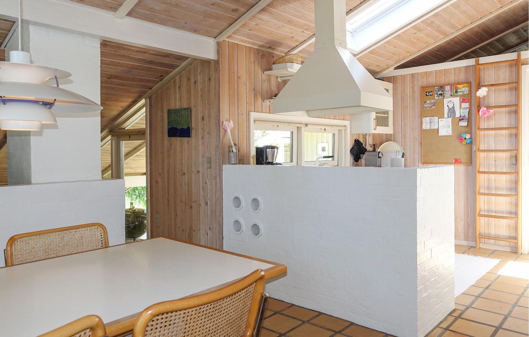 Cozinha moderna com detalhes em madeira, uma ilha branca e uma área de refeições com cadeiras de vime.