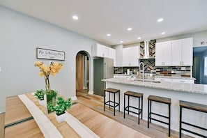 Uma cozinha moderna com armários brancos, backsplash em padrão herringbone e uma ilha central com banquetas.