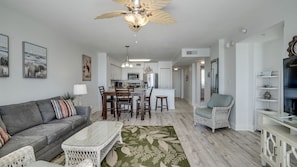 A modern living room with a grey sofa, a dining table with chairs, a wicker coffee table, and a ceiling fan.
