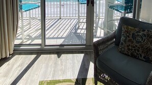 A balcony with a view of the ocean, a white table, and a wicker sofa with a cushion.