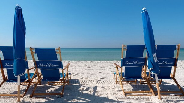 Four blue beach chairs with "Island Princess" branding on a sandy beach.