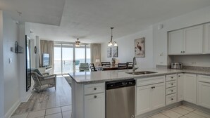 A modern kitchen with white cabinets, a dishwasher, and a dining area with a view.