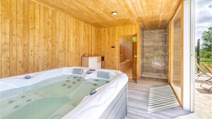 Uma cabana de madeira com banheira de hidromassagem, chuveiro e vista para o exterior.