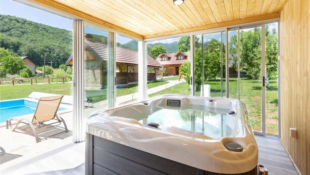 Uma área de spa moderna com hidromassagem, portas de vidro que dão para uma piscina e vista para uma paisagem montanhosa.