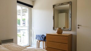 Ein Schlafzimmer mit Bett, Kommode, Spiegel und Fenster.