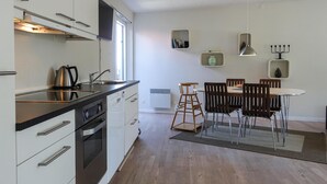 Eine moderne Küche mit Edelstahlgeräten, ein Essbereich mit rundem Tisch und Stühlen sowie eine kleine Sitzecke mit einer Stehleiter.
