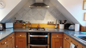 Una cocina equipada con estufa a gas, horno y microondas. Hay un reloj en la pared y una alacena con utensilios de cocina.