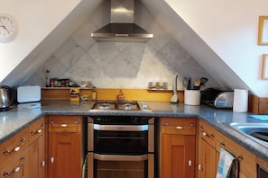 A kitchen with a gas stove, oven, and a microwave. There is a clock on the wall and a shelf with kitchen utensils. - 1 Bed Lodge - Sleeps 2 - Pets Ok - Free Parking (Acharacle)