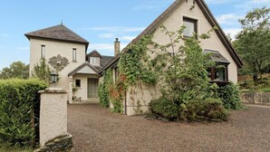 Una casa de dos pisos con una chimenea de piedra, un garaje pequeño adosado y un camino de entrada de grava.