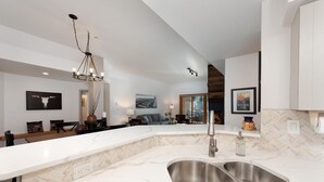 A modern kitchen with a large island, stainless steel sink, and a herringbone tile backsplash.