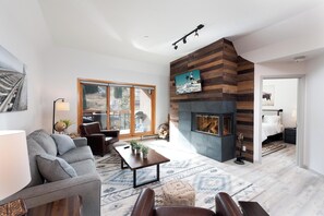 A modern living room with a fireplace, a sofa, a coffee table, and a large window. - Modern Village Center Ski In/Out Condo with Slope Views (Durango)