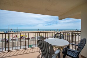 A balcony with a view of the beach, a round table, and two chairs.