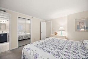 Une chambre à coucher avec un lit, une table de chevet, une lampe, un miroir et une armoire.