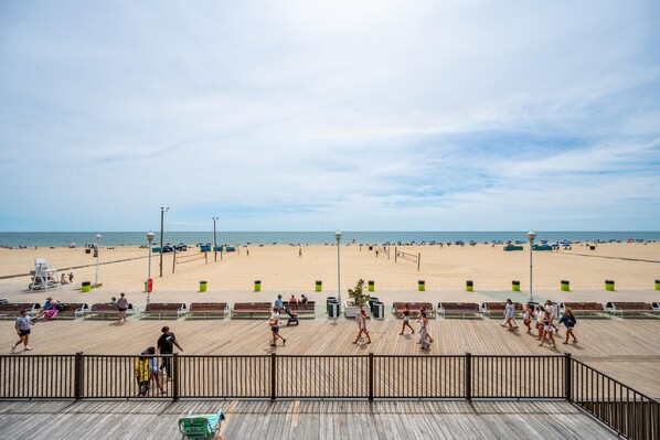 A beach with a wooden boardwalk, benches, trash bins, and people walking. - 2 br 2 bath, ocean and boardwalk front at 3rd St / large balcony (Ocean City)