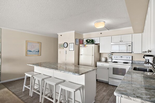 A kitchen with white cabinets, a marble countertop, a refrigerator, a microwave, an oven, and a sink.