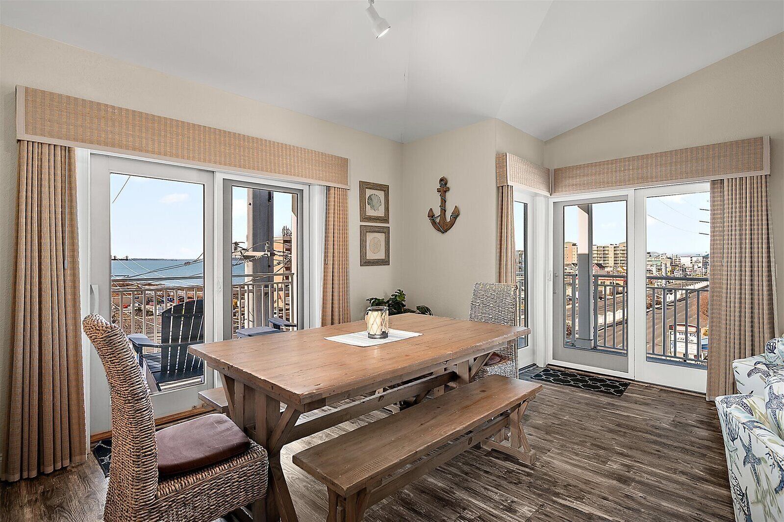 A room with a wooden table, wicker chairs, a bench, and large windows offering a view of the city.
