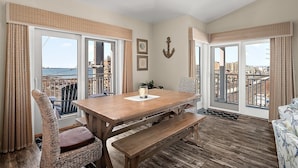 A room with a wooden table, wicker chairs, a bench, and large windows offering a view of the city. - 4100 Bldg - 3 Br 2 baths, outdoor pool. close to Convention Center, Night life and restuarants occ 10 (Ocean City)