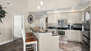 A modern kitchen with white cabinetry, stainless steel appliances, a central island, and a dining area with a wooden bench. - 4100 Bldg - 3 Br 2 baths, outdoor pool. close to Convention Center, Night life and restuarants occ 10 (Ocean City)