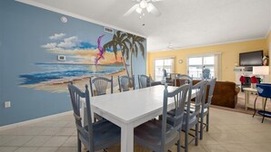 A dining area with a mural of a beach scene, a ceiling fan, and a kitchen area with a TV and counter. - 3 br oceanview 45th St with pool (Ocean City)