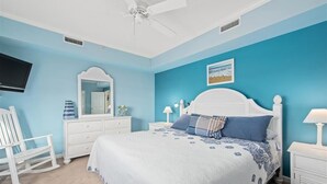 A bedroom with a bed, a white rocking chair, a dresser, a nightstand, a lamp, and a ceiling fan. - 3 br oceanview 45th St with pool (Ocean City)
