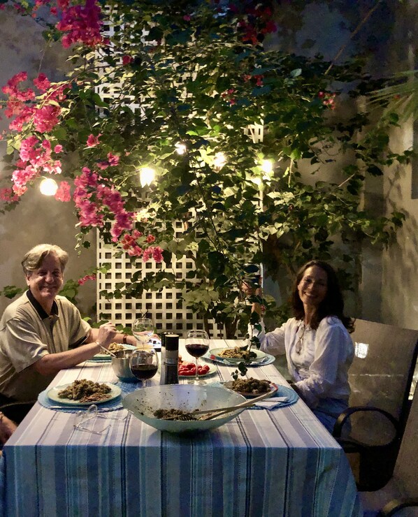 A dining table with plates of food and wine glasses, surrounded by a white lattice fence and flowering vines.